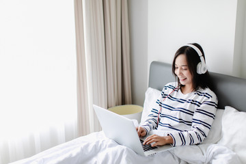 Caucasian woman sitting and playing with laptop on her bed in white bedroom