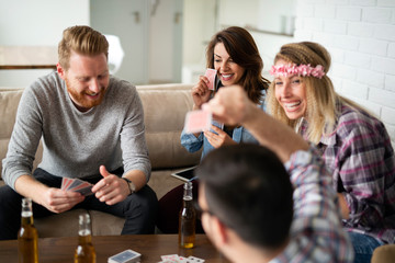 Group of happy friends playing cards and drinking