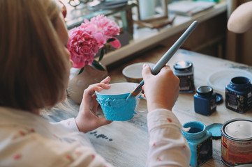 Woman working In her pottery studio. Ceramic workshop. Paint on clay mug in the pottery.