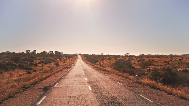 Legendary RN7 - stands for Route Nationale - road going through wild red African savanna with small trees and bushes on sides, at region near Ilakaka, sun shines in background