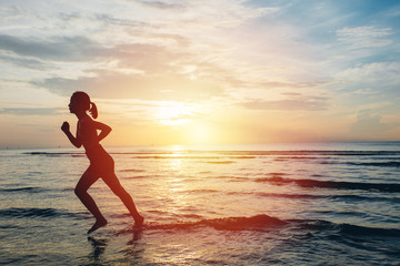 Fototapeta na wymiar Silhouette of an athletic woman running on the beach during sunset time