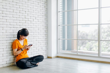 Happy beautiful woman sitting on the floor and using smartphone