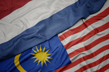 waving colorful flag of malaysia and national flag of netherlands.