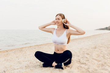 Fototapeta na wymiar sporty girl sitting on the beach and listening to music in headphones, after a workout
