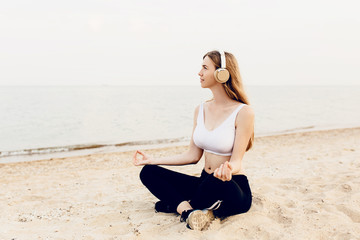 Fototapeta na wymiar Young athletic girl, meditating outdoors at sea, and listening to music