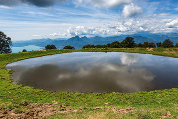 Small pond for livestock with reflections. In the background the Lake Garda and the Alps. Monte Baldo, Verona province, Veneto, Italy, south Europe
