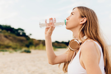 Close-up of tired young girl drinking water from bottle after workout