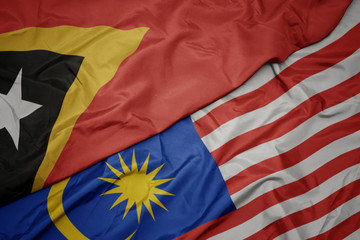 waving colorful flag of malaysia and national flag of east timor.