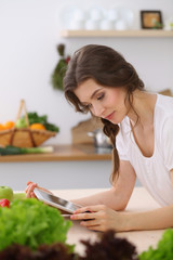 Young woman looking for a new recipe for cooking in a kitchen. Housewife is making online shopping by tablet computer and credit card