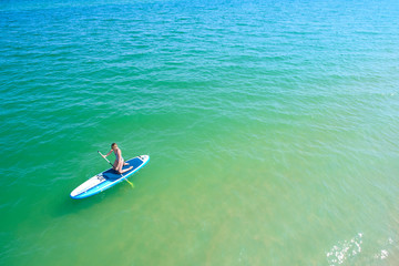 Young woman paddling on SUP board on the tropical beach. Active summer vacations with paddle board.