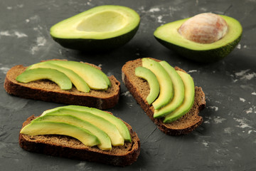 A sandwich of bread and slices of avocado on a black concrete background. making sandwiches.