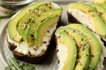 A sandwich of cream cheese bread, and slices of avocado on a plate on a light concrete background. making sandwiches. close-up