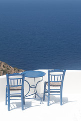 Fototapeta na wymiar Greece, the island of Sikinos. Two traditional taverna chairs and a blue table. In the background, the blue Aegean sea. Picture taken at a cafe high above the waters. Peace, simplicity and nature.