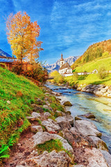 Fototapeta na wymiar Autumnal scenery of Ramsau National Park in Berchtesgadener Land in Bavaria, Germany. Incredible Alpine seasonal view of Parish Church of St. Sebastian. River Ramsauer Ache flowing Germany, Austria.