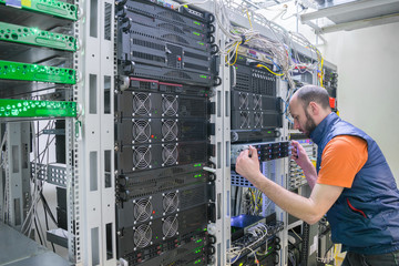 System administrator installs a new server in a modern data center. Specialist makes a backup copy of the computer database. Technician repairs the central router in the datacenter server room.