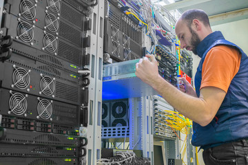 A man works in a server room. System administrator installs a new server in a modern data center. A technician repairs the central router.
