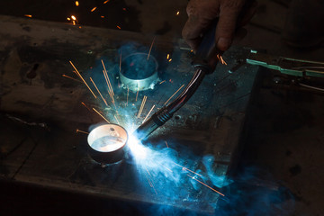 Semi-automatic spot welding of metal parts during the work of the master in the construction workshop with blue smoke and yellow sparks.