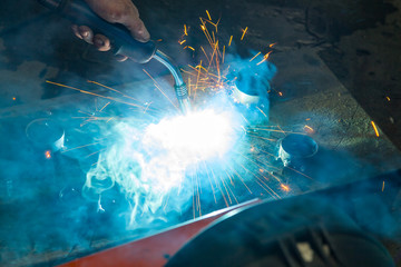 Semi-automatic spot welding of metal parts during the work of the master in the construction workshop with blue smoke and yellow sparks.