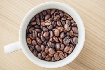 fresh roasted coffee beans in white cup on wood table, top view