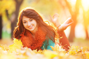 Young pretty woman relaxing in the autumn park. Beauty nature scene with colorful foliage background, yellow trees and leaves at fall season. Autumn outdoor lifestyle