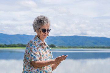 Senior woman stand holding mobile at side the lake