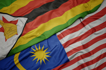 waving colorful flag of malaysia and national flag of zimbabwe.