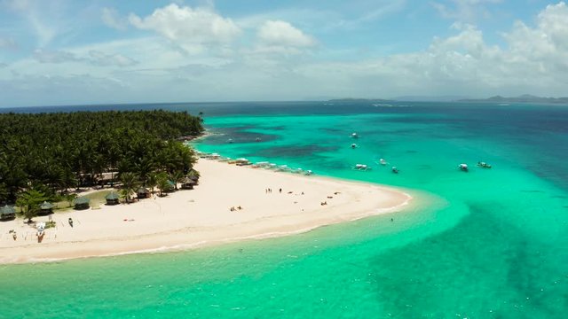 Sandy beach with tourists, palm trees and turquoise water on the island of Daco, Philippines, aerial view. Summer and travel vacation concept