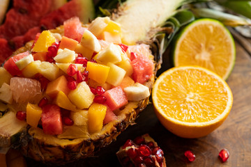 Close up fruit salad served in half pineapple on a rustic wooden table. Gourmet food. Tropical fruit. Diet healthy food, nutrition. Fresh Juicy natural fruit.