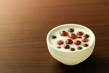Fresh juicy grape and homemade yogurt in a white bowl on dark brown wooden background.