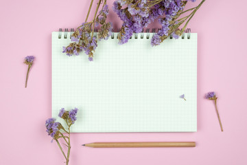 Top view of blank notebook and flower on pink background
