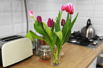 Tulips bouquet in your home standing on a wooden countertop in the kitchen. Modern white u-shaped kitchen in scandinavian style.