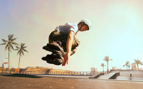 Rollerskater man is performing tricks in skatepark on sunset.