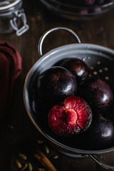purple plums in gray colander on dark wooden background