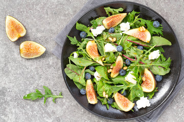 Fig salad with goat cheese, blueberry, with pine nuts and arugula on grey background. Vegetarian food. Top view. 