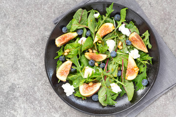 Fig salad with goat cheese, blueberry, with pine nuts and arugula on grey background. Vegetarian...