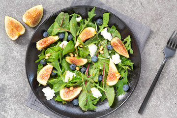 Fig salad with goat cheese, blueberry, with pine nuts and arugula on grey background. Vegetarian food. Top view. 