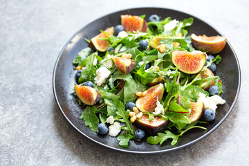 Fig salad with goat cheese, blueberry, with pine nuts and arugula on grey background. Healthy food. Vegetarian food. Close up