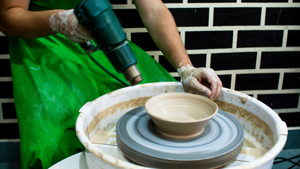 A raw clay pot in the hands of a potter. Workshop in the pottery workshop. Clay pot on a potter`s wheel