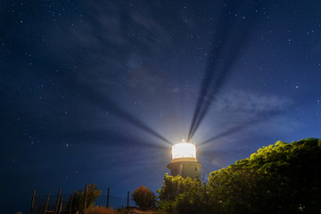 White sea lighthouse in Feodosia, Crimea on the Black Sea with rays of light under the night sky