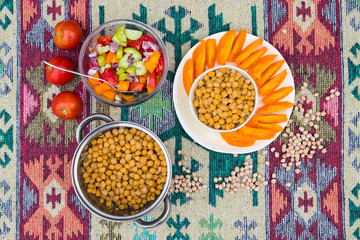 Homemade cooked chickpea bowl and steel pan with vegetables (tomatoes).