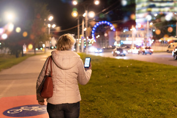 Fototapeta premium A woman with a mobile phone in her hand is walking through the night city.