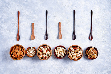 pecans, hazelnuts, almonds, pine nuts, cashews in wooden bowls on blue background, top view, flat...