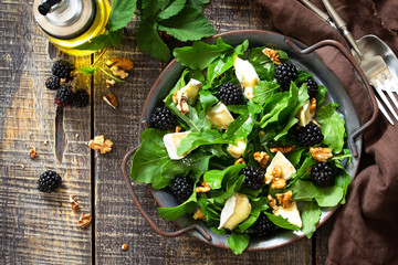 Diet menu, Vegan food. Healthy salad with arugula, brie cheese, nuts and vinaigrette dressing on a rustic wooden table. Top view flat lay.