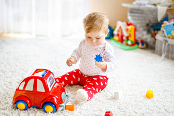 Adorable cute beautiful little baby girl playing with educational wooden toys at home or nursery. Healthy happy toddler with colorful red car indoors. child learning colors and forms