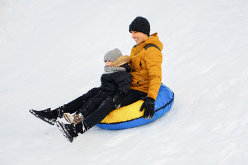 Fototapeta na wymiar Happy dad and son are sliding from snow hill at tubing. Winter outdoor activity.
