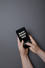 Black Friday Sale online shopping, holding mobile phone and touching the screen with fingers, flat lay on dark gray background