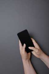 Holding mobile phone in hands and touching the screen with fingers, flat lay on gray background