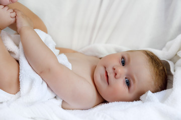Fototapeta na wymiar Cute little baby playing with own feet after taking bath. Adorable beautiful girl wrapped in white towels