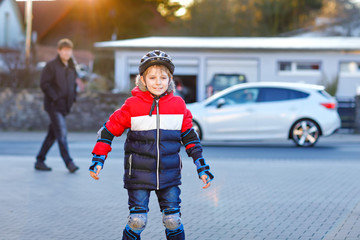 School kid boy and father skating with rollers in the city. Happy healthy child in protection...