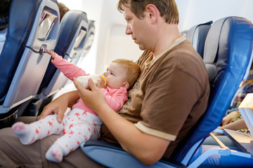 Father holding his baby daughter during flight on airplane going on vacations